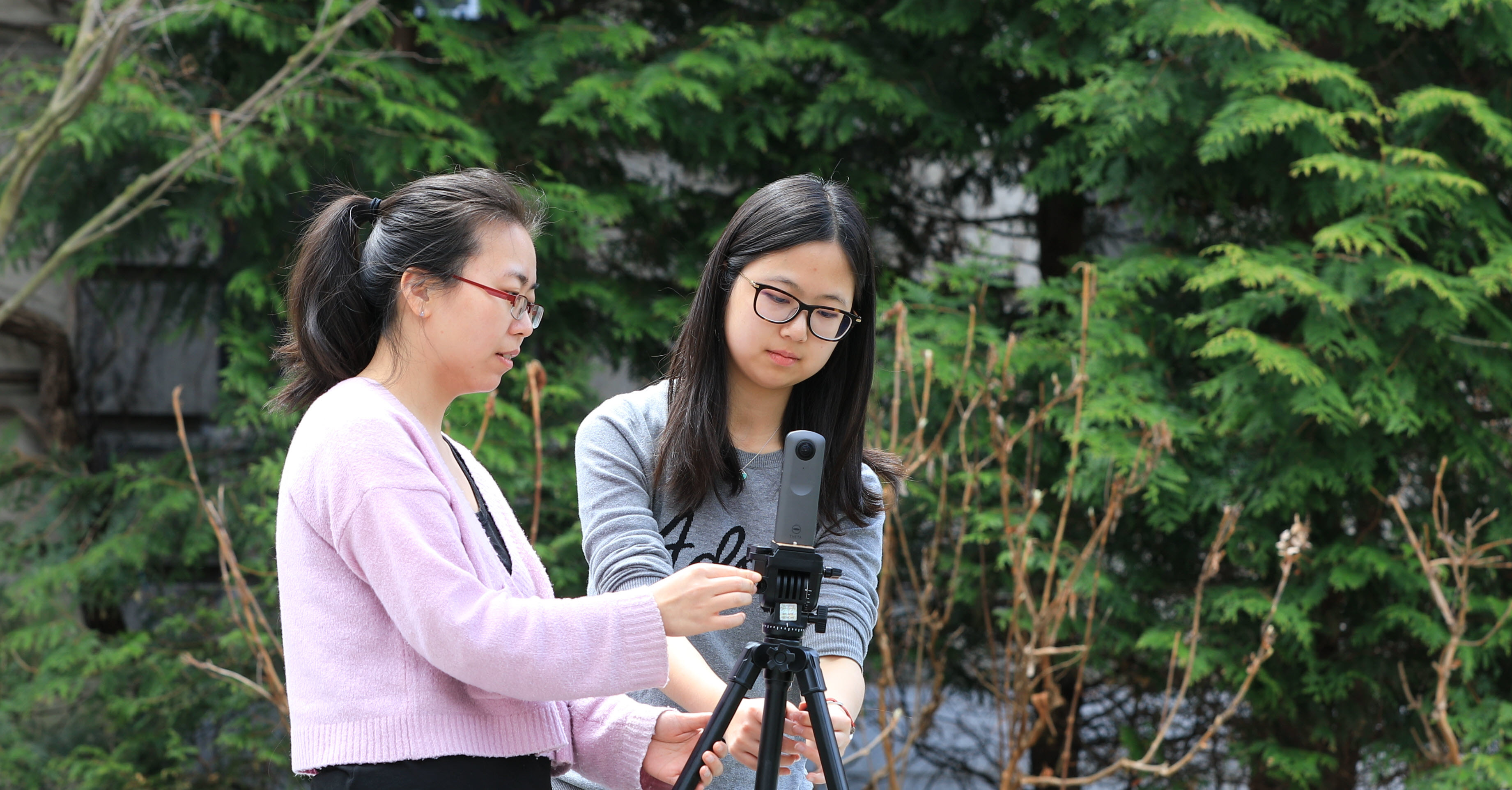 Students setting up camera for outdoor filming with trees in background