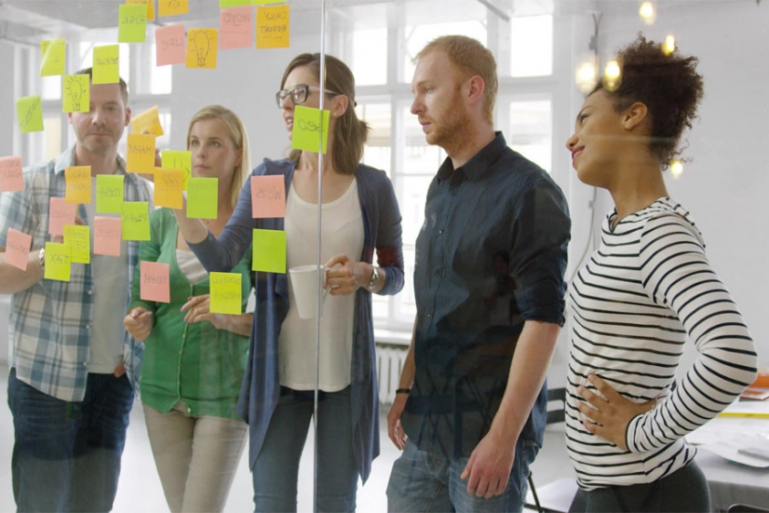 A group of five students placing notes on a glass surface