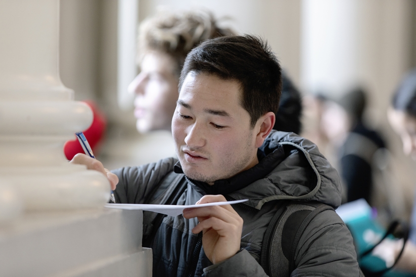 A student writes on a worksheet, propped against wall