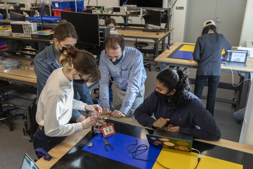 Instructor Benjamin Finio observes while Molly Drumm, Emily Harmon, and Sunaya Reddy work on their robot in the lab