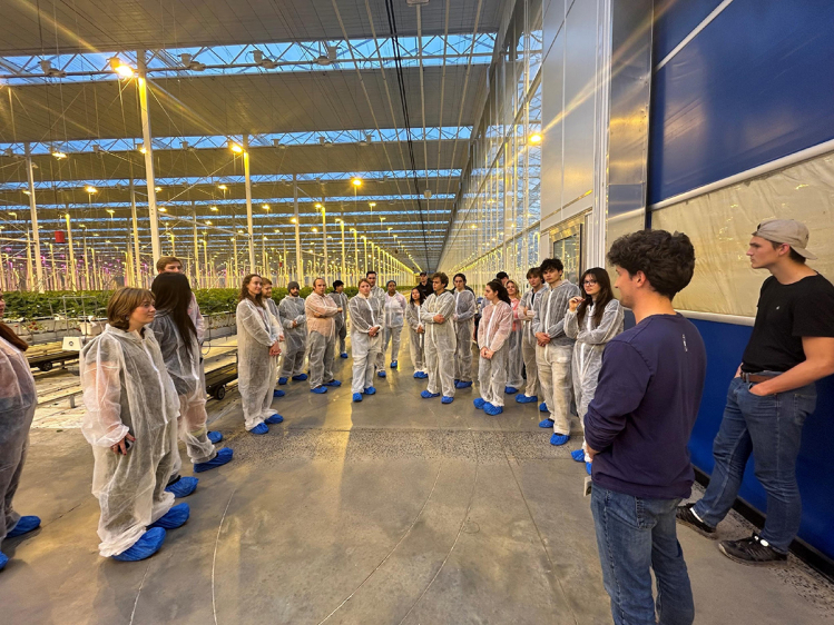 Students wearing protective suits gather in a semicircle during a visit to Green Empire Farms’ 32-acre strawberry greenhouse operation
