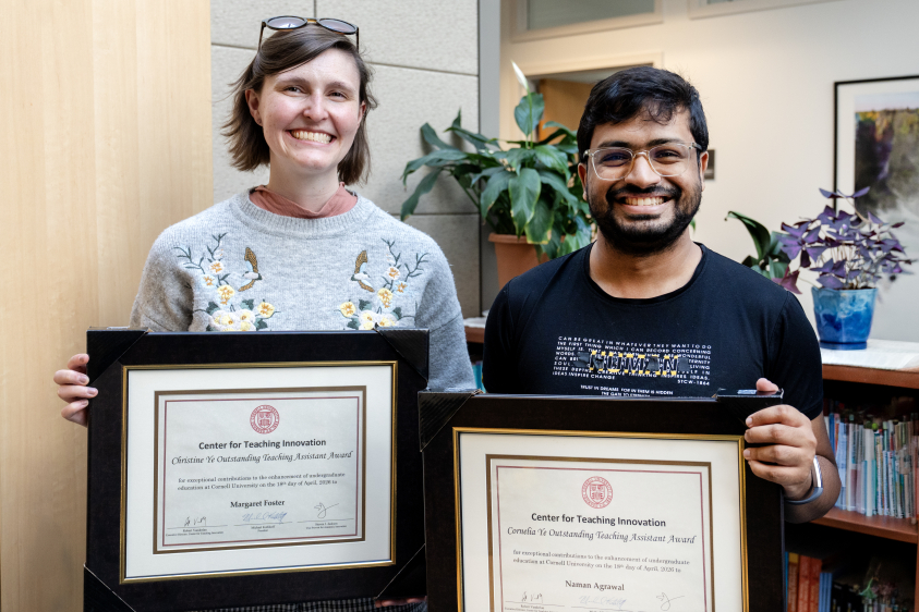 A woman in a grey sweater and a man in a navy shirt hold their award certificates for excellence in graduate teaching.