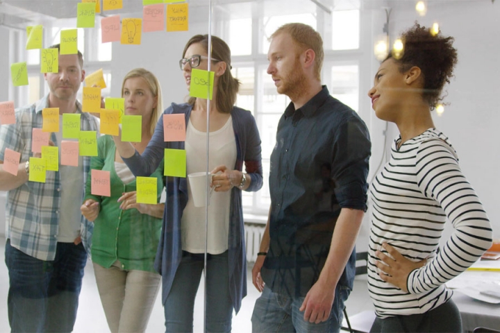 A group of five students placing notes on a glass surface