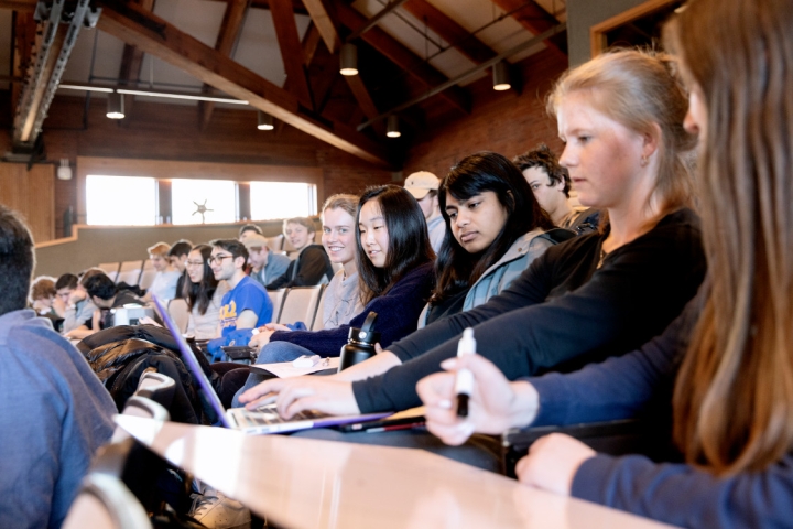 students sitting around a computer in large lecture hall.