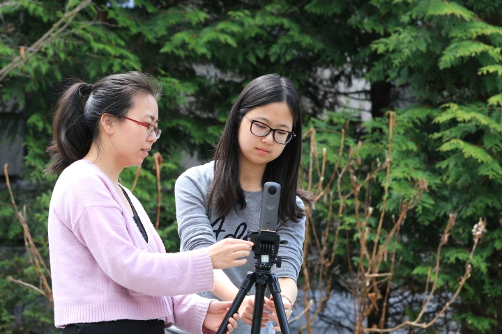 Students setting up camera for outdoor filming with trees in background