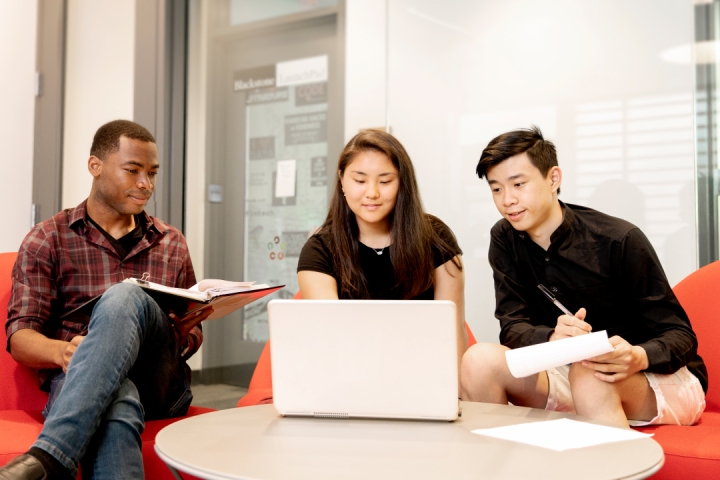 three students sitting around a laptop