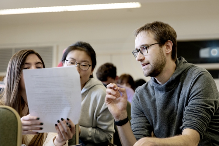 A teaching assistant engages with students' questions in the classrooom.
