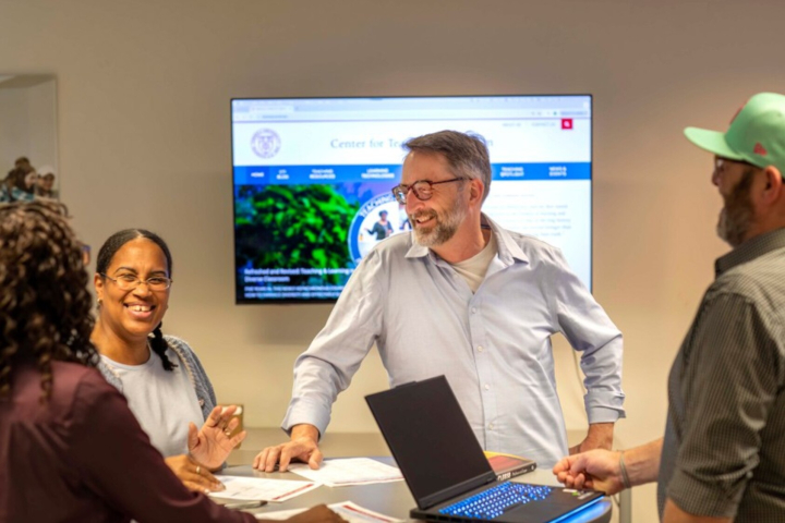 A brown-haird man in a white shirt and glasses engages in classroom discussion