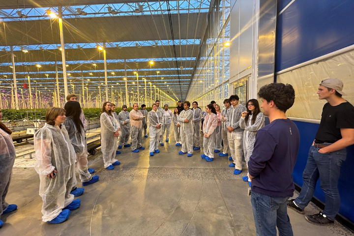 Students wearing protective suits gather in a semicircle during a visit to Green Empire Farms’ 32-acre strawberry greenhouse operation