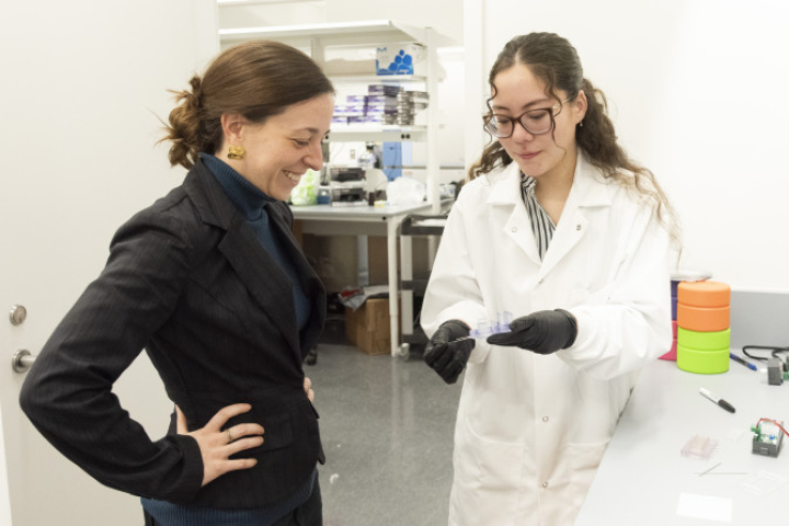 A female professor assists a young female engineering student in a white lab coat