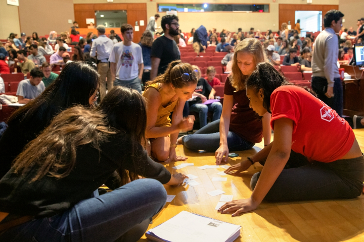 A group of five students collaborate on a group project using index cards