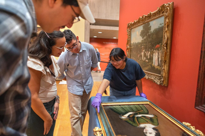 Three students gather around a portrait with a museum curator