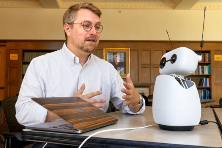 A male professor talks to a small white robot